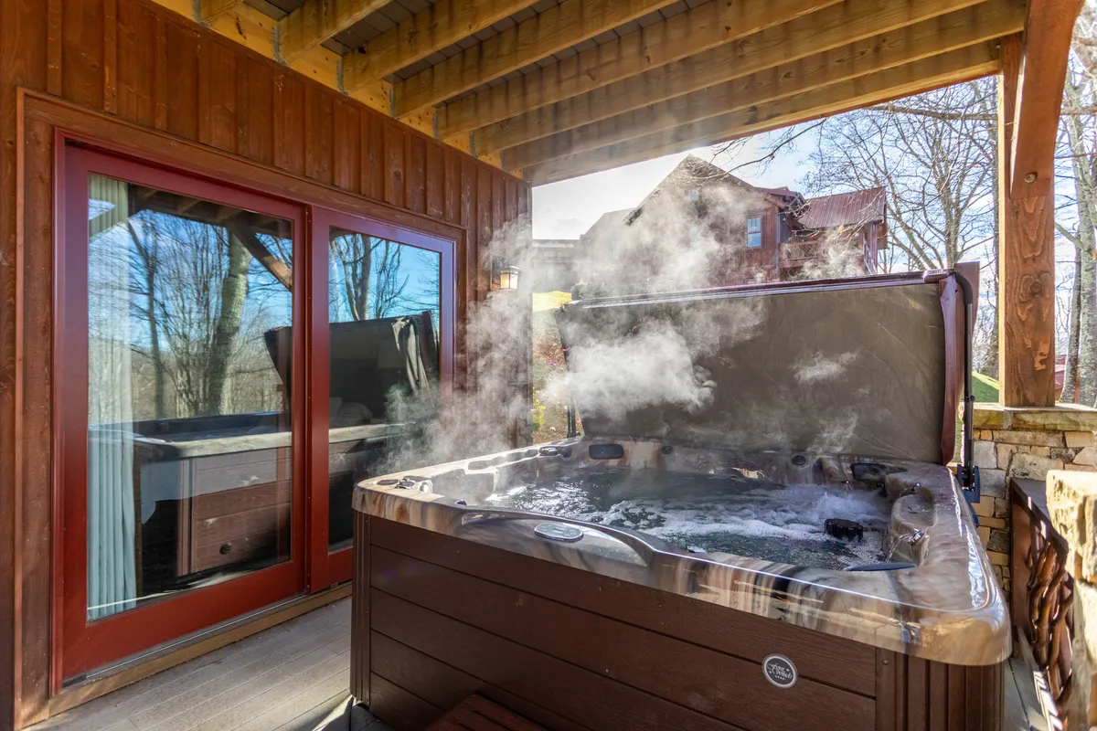 An outdoor hot tub surrounded by trees and large windows, offering tranquil views and an inviting place to soak under the open sky. The setting transitions indoor comfort to outdoor relaxation, ideal for post-adventure stargazing or unwinding.