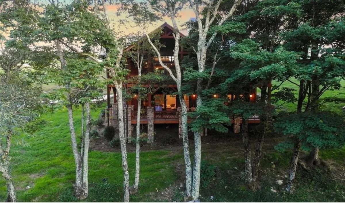 This exterior shot captures the wooden structure of the home nestled among tall trees. The soft glow from interior lights spills onto the porch, creating a tranquil scene perfect for relaxing after outdoor activities. The surrounding nature invites exploration of nearby trails.