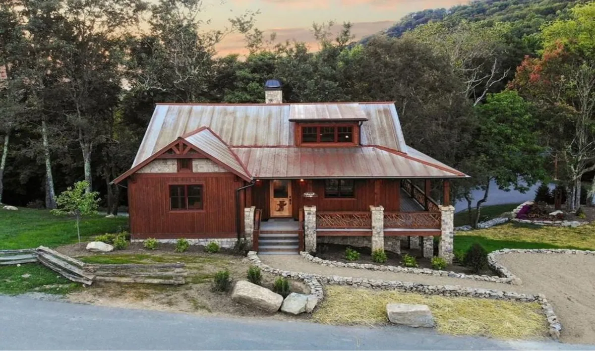 This image showcases the rustic wooden exterior of Timberwolf Lodge, featuring a metal roof, sturdy stone pillars, and a welcoming front porch set against a backdrop of natural surroundings. The twilight lighting hints at the possibilities for evening gatherings or relaxation after a day of adventure.