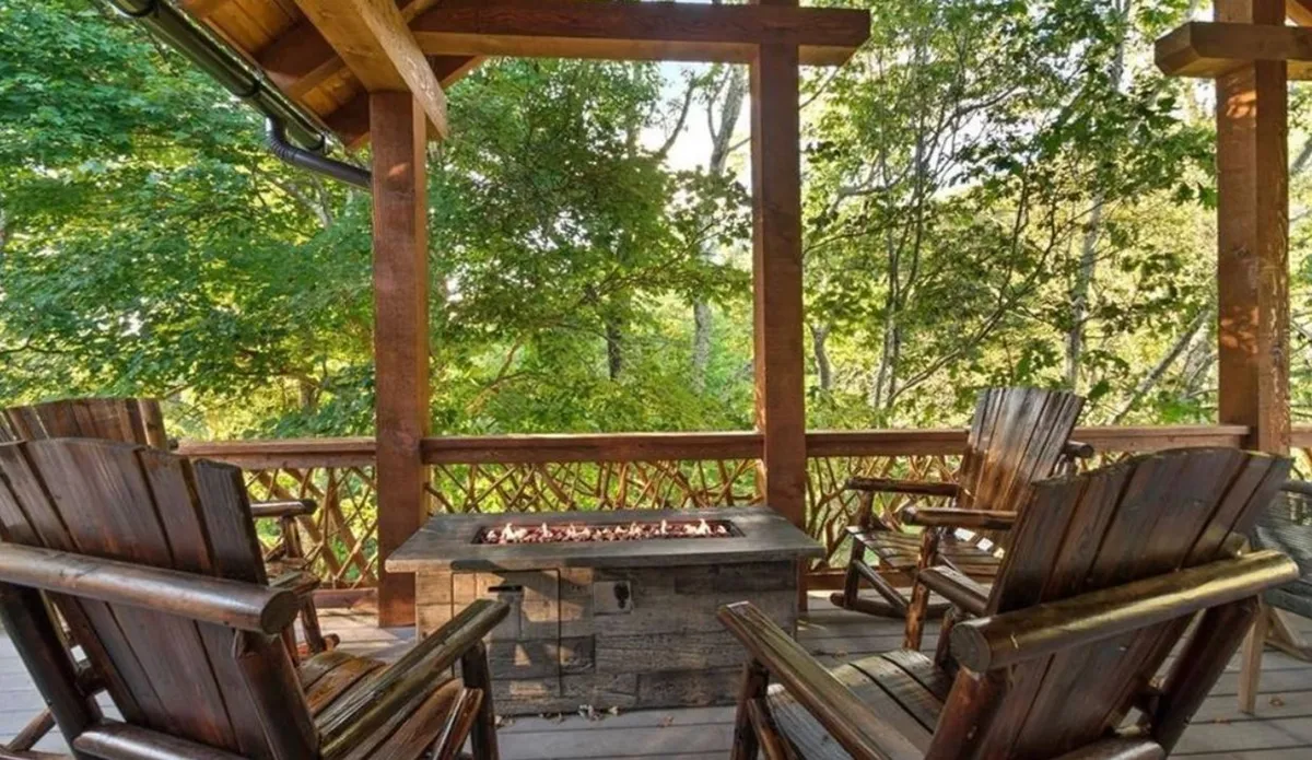 A cozy outdoor fire pit area surrounded by wooden rocking chairs and lush greenery. The scene invites guests to relax, share stories, or roast marshmallows as the sun sets, creating a warm gathering place for families.