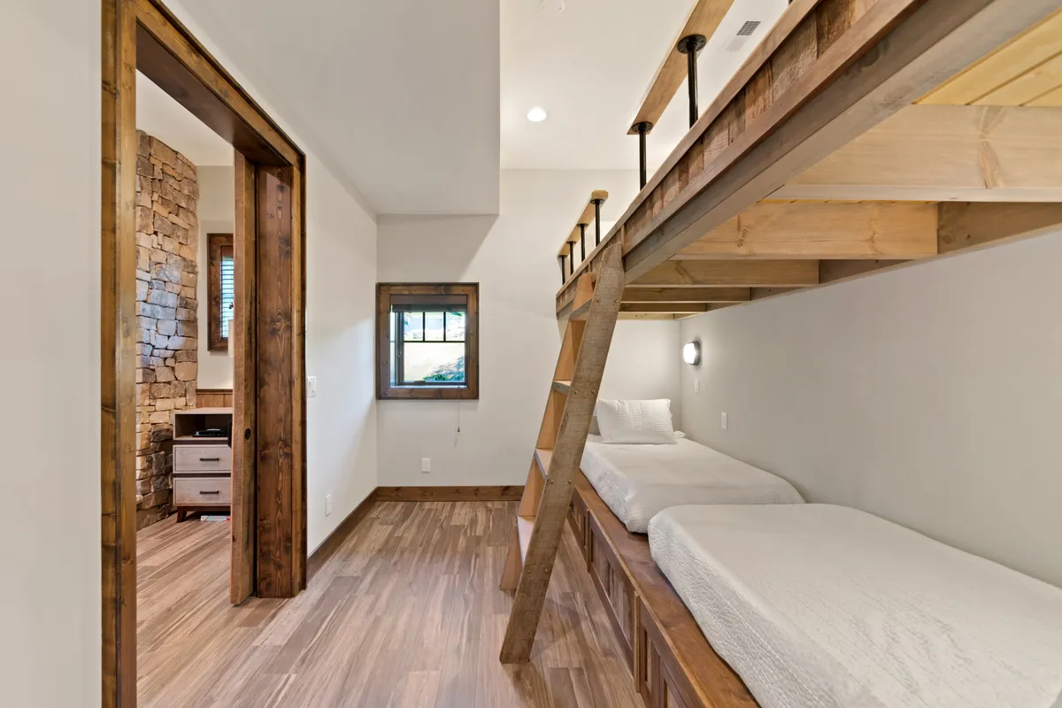 A tranquil bunk room with a cozy bunk bed set against a textured stone wall and a window offering scenic views. The mood is restful and inviting, ideal for unwinding after a day of adventure.
