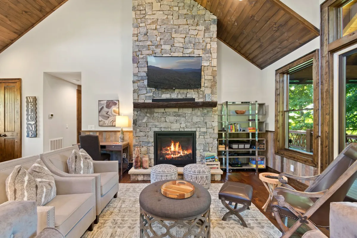 A welcoming lower-level lounge featuring a stone fireplace, plush comfortable seating, warm wooden accents, and large windows that fill the room with natural light. The scene evokes a sense of relaxation and communal enjoyment, perfect for movie nights, board games, or gathering after a day of adventure.