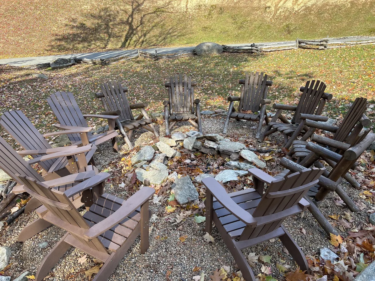 A cozy fire pit is surrounded by comfortable chairs, set in a leafy outdoor space with autumn colors. The setting is ideal for group gatherings, sharing stories, and unwinding under the stars, capturing the sense of community and relaxation.