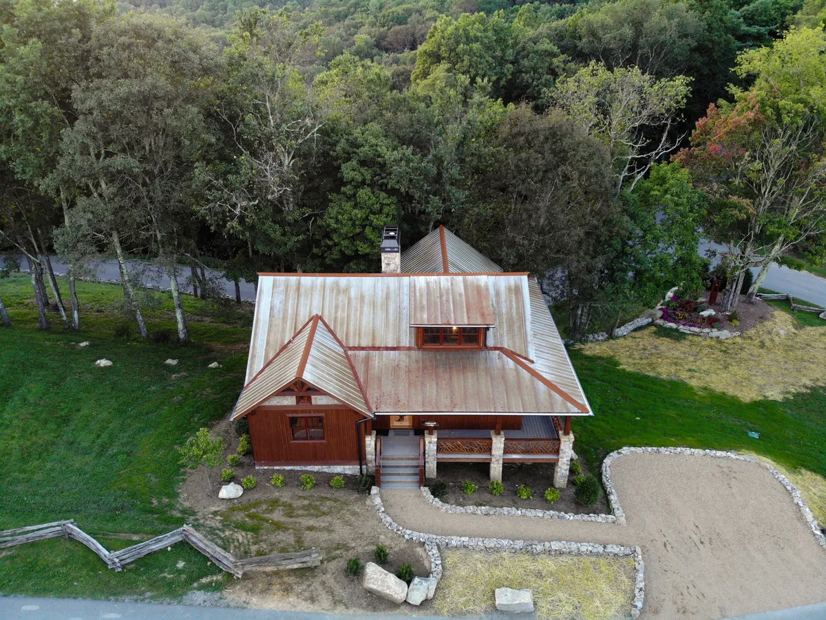 This image showcases the rustic wooden house nestled among landscaped yards and mature trees, with a stone path leading to the entrance. The warm tones of the sunset create an inviting glow, highlighting the peaceful ambiance and natural beauty of the surroundings.