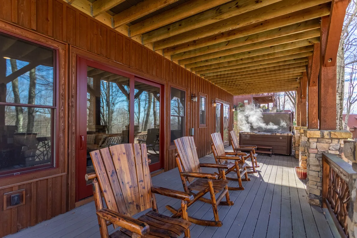 A welcoming patio featuring a hot tub, wooden rocking chairs, and large glass doors opening onto the natural surroundings. The scene suggests relaxation and socializing after a day of adventure, with the hot tub as a standout feature.